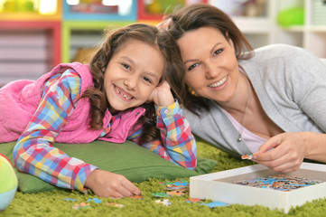 Fototapeta premium Close up portrait of mother with little daughter collecting puzzle
