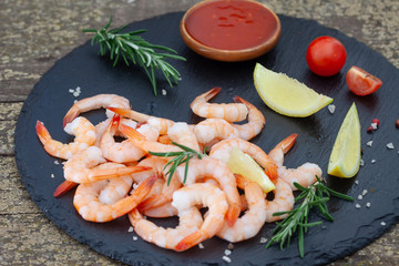 Shrimps with fresh lemon, cherry tomato and rosemary on black plate. Shrimp tailes with spices.
