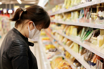 Woman in medical mask choosing food products in a superstore. Concept of shopping during quarantine at covid-19 pandemic