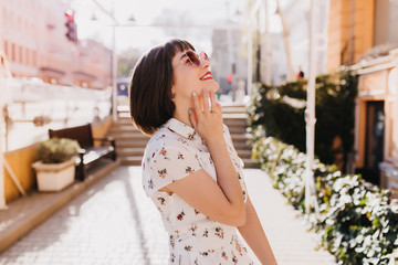 Romantic brown-haired woman smiling on street background in weekend. Outdoor shot of refined female...