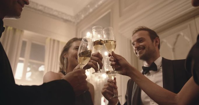 Wealthy people holding the glasses of white wine making a toast at party. Group of people enjoying a cozy evening with drinks.
