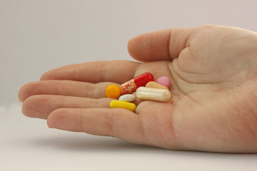 Tablets of different colors and shapes lie in palm of your hand. Palm of the whole. Tablets of red, white, yellow, pink. Located on the left. Taking drugs. Treatment. Home first aid kit.