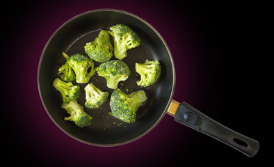 Green frozen broccoli in a pan, on black background
