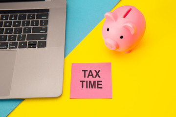 Tax time - notification of the need to file tax returns, tax form at accauntant workplace. Piggy bank in pink color with laptop and stationery on colorful background.