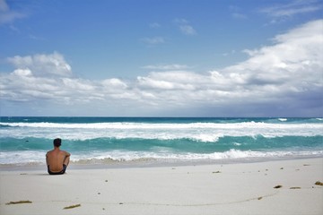 A man sits on a wild ocean beach