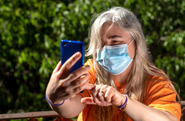 Woman in surgical mask taking selfies during confinement due to coronavirus