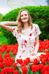 Portrait of a young beautiful girl in a summer dress posing on the lawn with red tulips