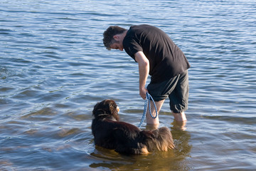 Dunkelhaariger Mann mit schwarzem Hund krempelt im Meer seine Hose hoch