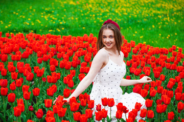 Portrait of a young beautiful girl in a summer dress posing on the lawn with red tulips