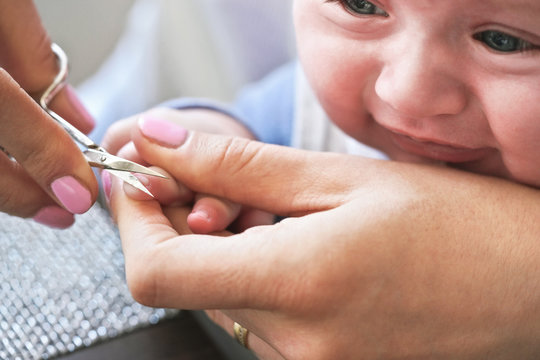 Infant baby boy having his nails cut by mother, detail on scissors and fingertips