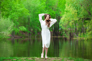 Fototapeta na wymiar Portrait of a young beautiful woman in white dress posing by the lake