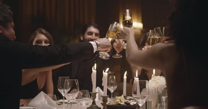 Young man raising his glass of wine with friends at party. Group of people enjoying dinner at a gala night.
