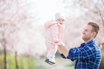 A young dad holds in his arms a small pretty daughter. Dad and daughter in a flowered garden. Sakura.