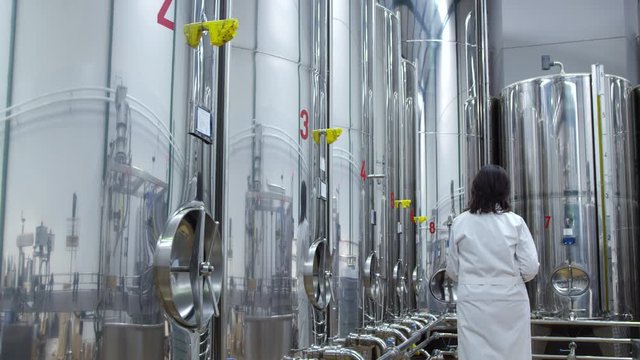 WS DS Woman in lab coat with clipboard walking along storage tanks
