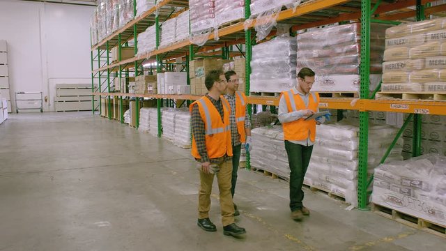 WS&nbsp;DS&nbsp;TS Three workers walking and talking in Warehouse, Drywall with one holding tablet