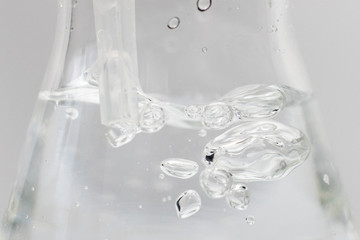 Closeup of a liquid with bubbles in a glass erlenmeyer flask with a plastic pipette in it on a...