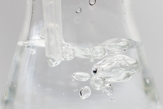 Closeup of a liquid with bubbles in a glass erlenmeyer flask with a plastic pipette in it on a white background. Science experiment.