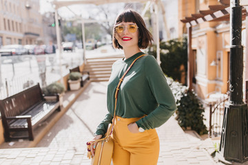 Laughing romantic girl in green sweater enjoying sunny spring day. Gorgeous short-haired woman in sunglasses chilling in weekend.