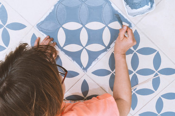 Home improvement concept: Top view of a femal painting tiles into blue using a vintage design...