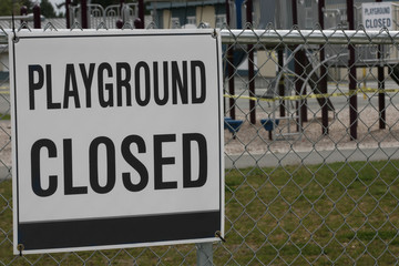 Horizontal color photograph of a "playground closed" sign in front of a vacant school yard