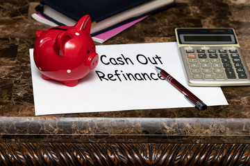 Paper with the words cash out refinancing on a table next to a red piggy Bank.