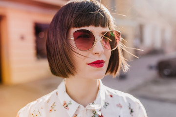 Close-up shot of magnificent european girl in white blouse. Outdoor photo of adorable woman in dark sunglasses.