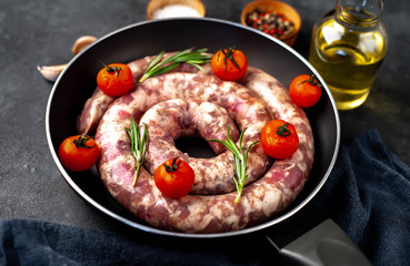 raw spiral sausage in a pan with spices and rosemary on a stone background