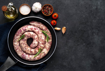 raw spiral sausage in a pan with spices and rosemary on a stone background with copy space for your text