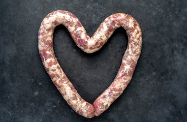 raw sausage with spices and rosemary laid out in the shape of a heart on a stone background with copy space for your text