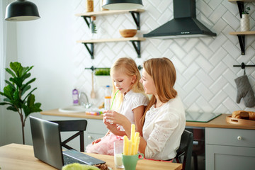 Young mother with daughter child at home in kitchen with a laptop at a table on Internet online learning to cook and shop