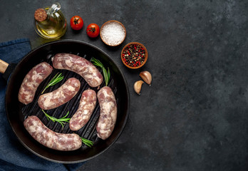 raw sausages in a pan with spices and rosemary on a stone background with copy space for your text
