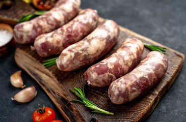 
raw sausages with spices and rosemary on
cutting board on stone background