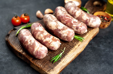 
raw sausages with spices and rosemary on
cutting board on stone background