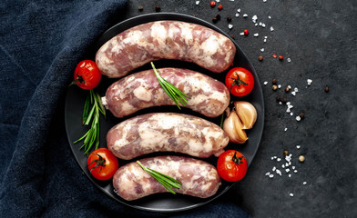 raw sausages with spices and rosemary on
plate on stone background