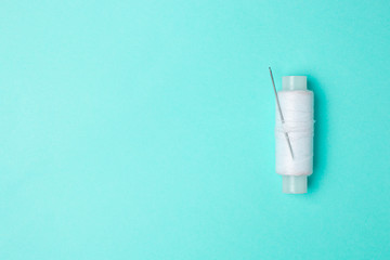 Spool of white thread with a needle on a blue background