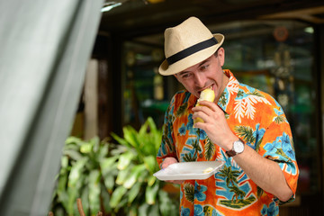 Young handsome tourist man eating durian in the city outdoors