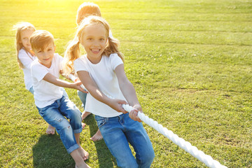 A group of children have fun playing in nature. Children jump over the rope. Warm summer evening...