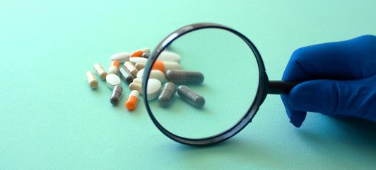 hand in blue medical glove holds magnifying glass looks at white round pill, close up, selective focus , blurred neutral background