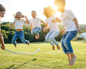 A group of children have fun playing in nature. Children jump over the rope. Warm summer evening...