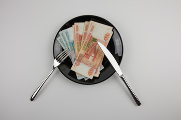 Paper Russian money on a plate, next to a fork and knife. Consumer culture. Money instead of food.