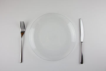 Transparent plate, metal fork and knife on a white background. Table setting. For presentation of dishes and restaurants.