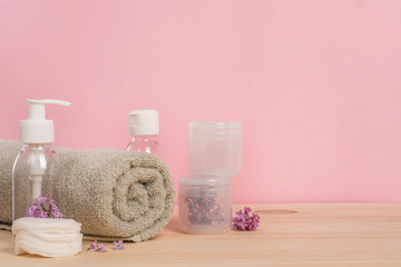 Obraz na płótnie Canvas Spa pink background, body and skin care with cosmetic bottles, towel and lilac flowers in a coconut bowl on a wooden table. beauty concept