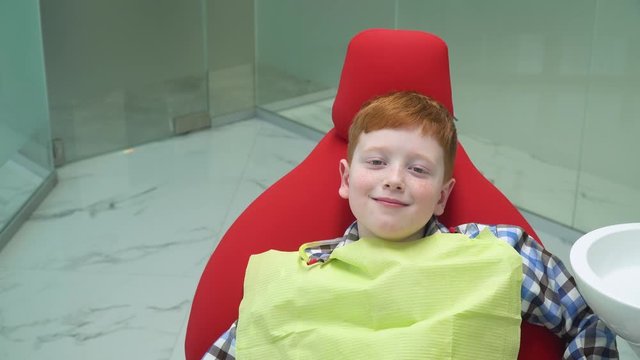 Happy red-haired boy at reception at dentist in dental chair that is down. Pediatric dentistry