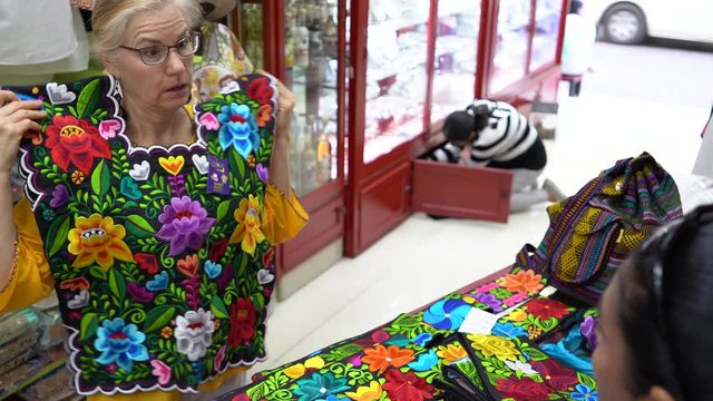 Closeup overhand view of mature woman wearing ethnic clothing looks at colorful cinturon belts in a shop in Merida, Mexico.