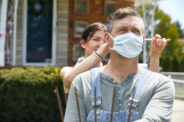 A wife lovingly ties a coronavirus facemask on her husband before work to safeguard from exposure...