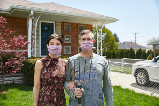 A Couple Stands In Solidarity Outside Their Home Wearing Coronavirus Facemasks To Prevent Expose To The Virus While Posing As The Famous Artwork American Gothic