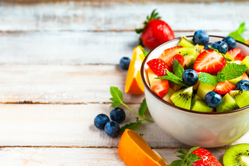Concept of low calories delicious desserts. Summer fresh bowl with colorful fruit salad. Healthy natural organic food. Tasty snack, light simple lunch. Wooden background close up copy space for text