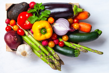 Wooden case with fresh ripe seasonal vegetables. Ingredients for cooking tasty light vegan meal. White background, close up, macro. Top view flat lay