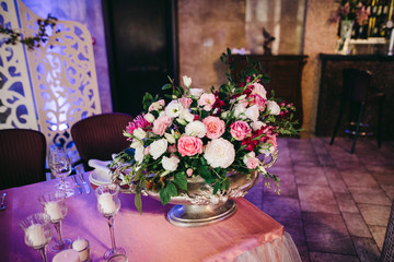 Festive stands in the wedding banquet area served with dishes and cutlery and decorated with compositions of flowers, greenery and candles