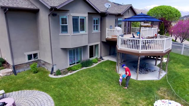 Aerial view of an urban home with grandmother and toddler granddaughter playing in the backyard - orbit movement